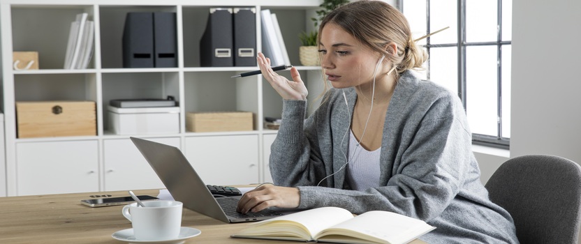 Mulher trabalhando em casa com laptop e caderno.