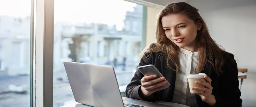 Mulher usando celular e laptop em café